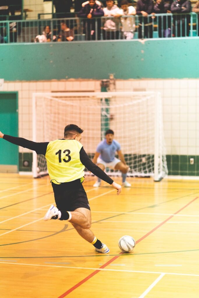 Home Player kicks the ball towards the goal in a competitive indoor futsal match.