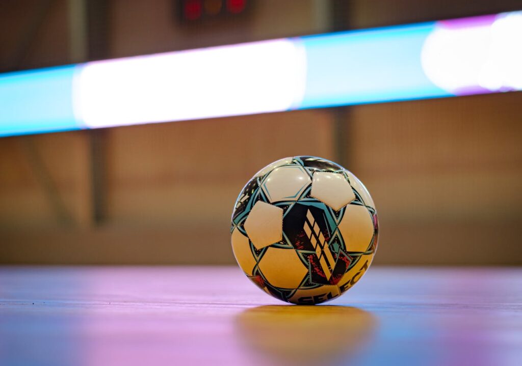 Home Close-up of a soccer ball on a gym floor with blurred background lights.